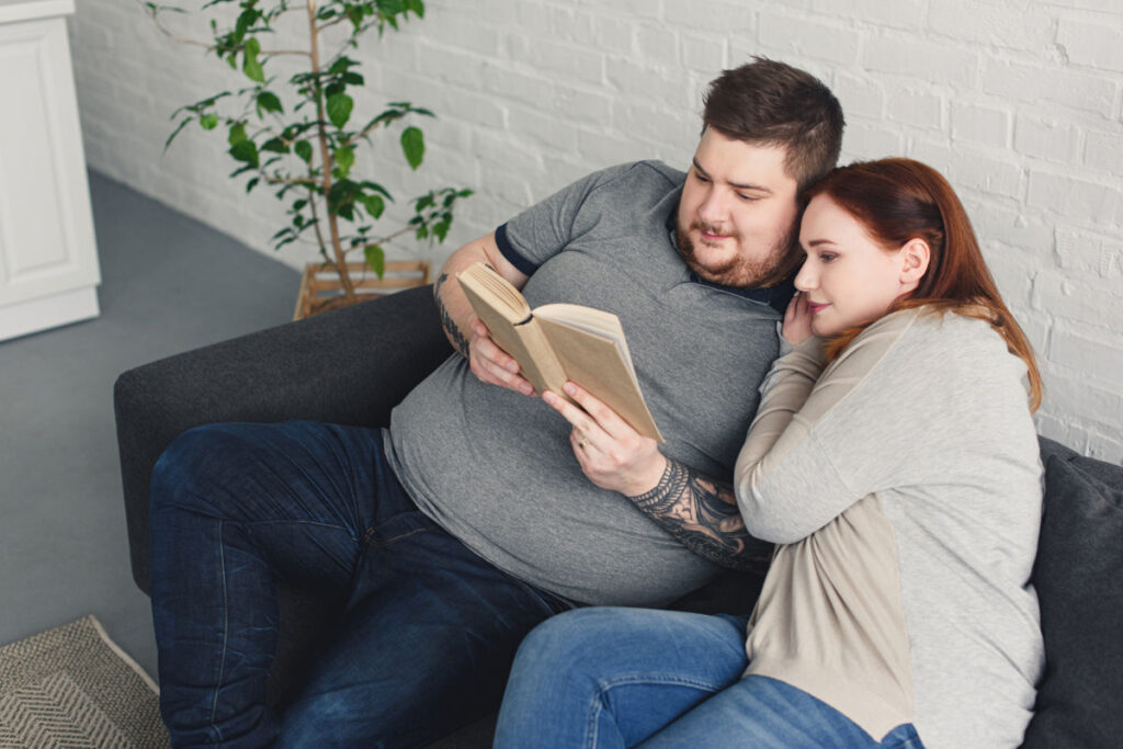 boyfriend and girlfriend reading book together on sofa in living room