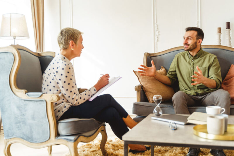 Smiling handsome young man in casual clothes sitting on a sofa during the therapy session