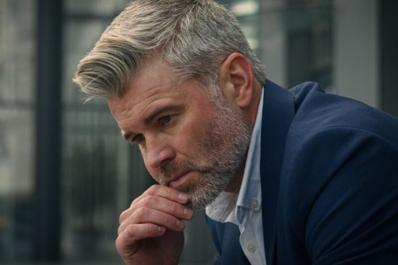 Pensive sad worried sorrowful thoughtful middle-aged man senior mature business employer businessman think ponder problem solution grief put on glasses dreaming contemplate thinking in city outdoors