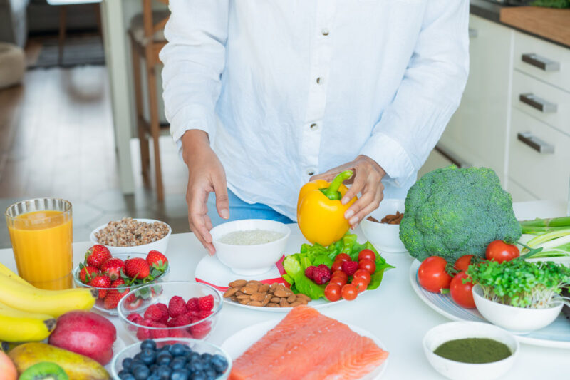 Female Nutritionist expert makes healthy balanced diet plate according to proportions of nutrients. Plate with pie chart of fruit, vegetables, grains, proteins on kitchen table with ingredients