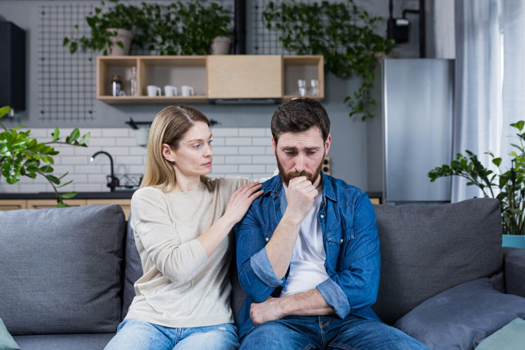 A woman supports an upset husband who has failed, a married couple sitting on the couch