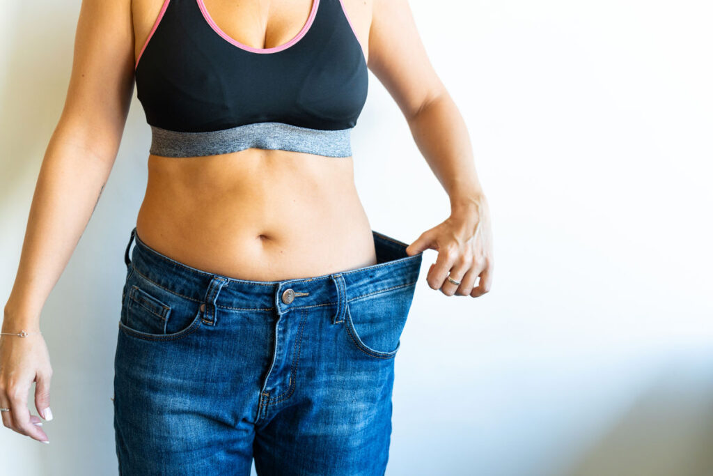 Woman wearing oversized jeans, proudly displaying successful weight loss achieved through dedicated dieting and consistent workouts